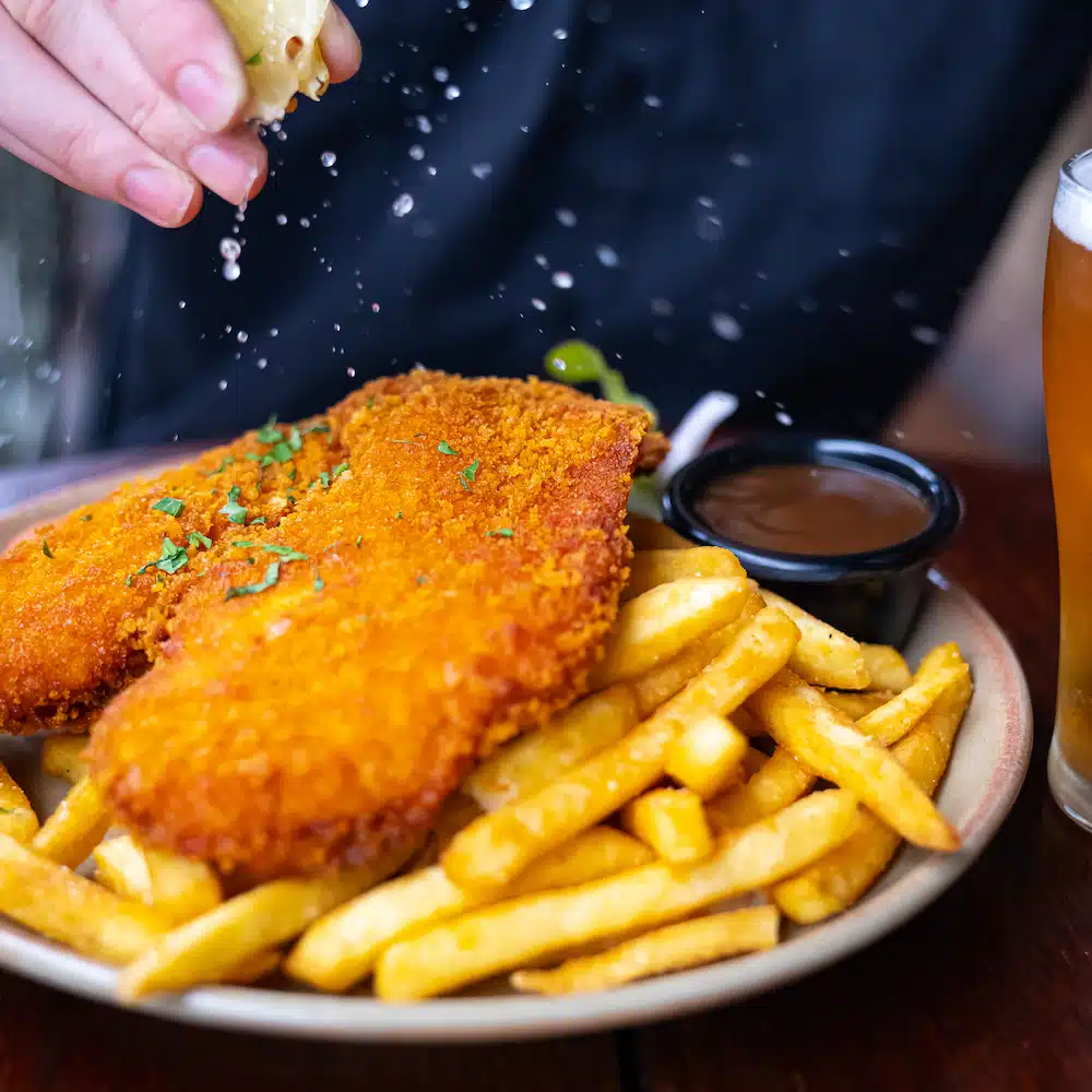 Schnitzel on a plate of chips with a cup of gravy