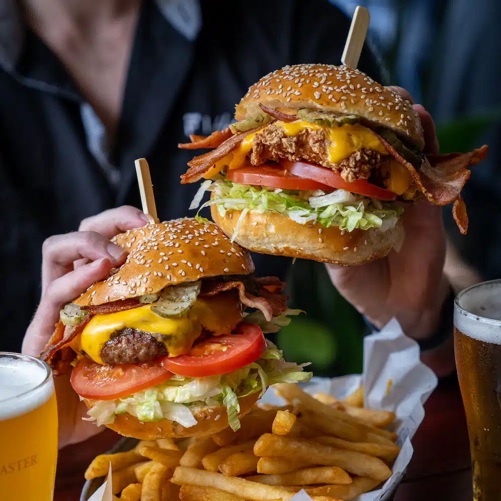 Two burgers being held in each hand over a plate of chips