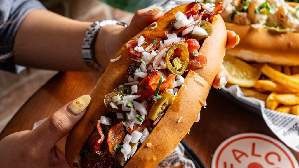 Wagyu beef and bacon with onions and jalapeños being held in hands